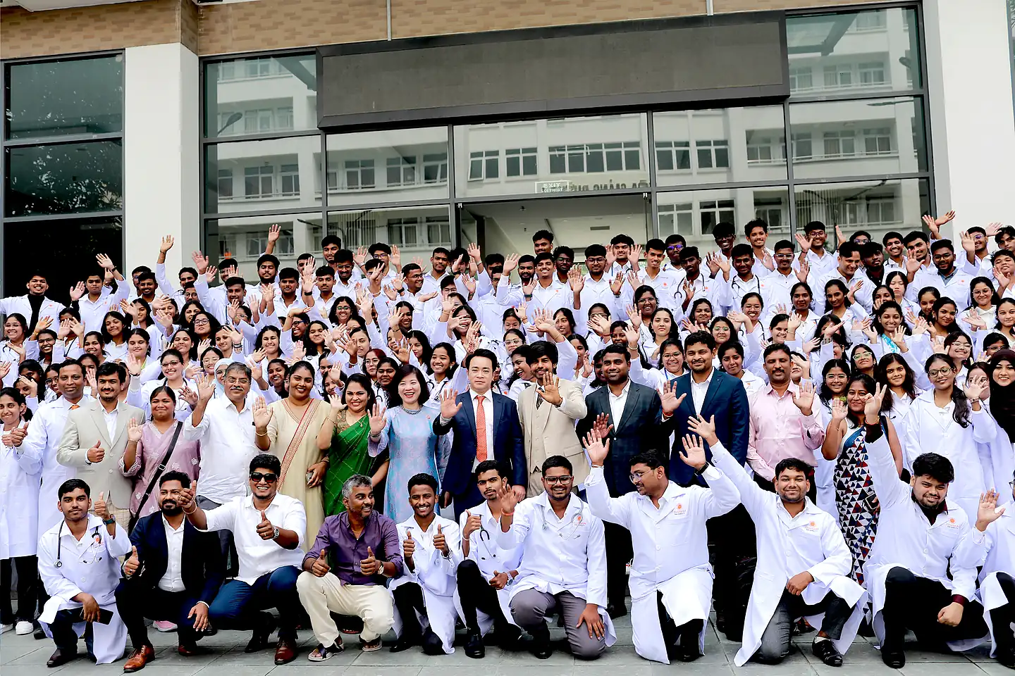 Large cohort of Indian MBBS students in white coats cheering with faculty at Dai Nam